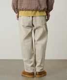 Back view of a model wearing sand pigment Gramicci EQT Pant and a plaid jacket on a light-tone background.