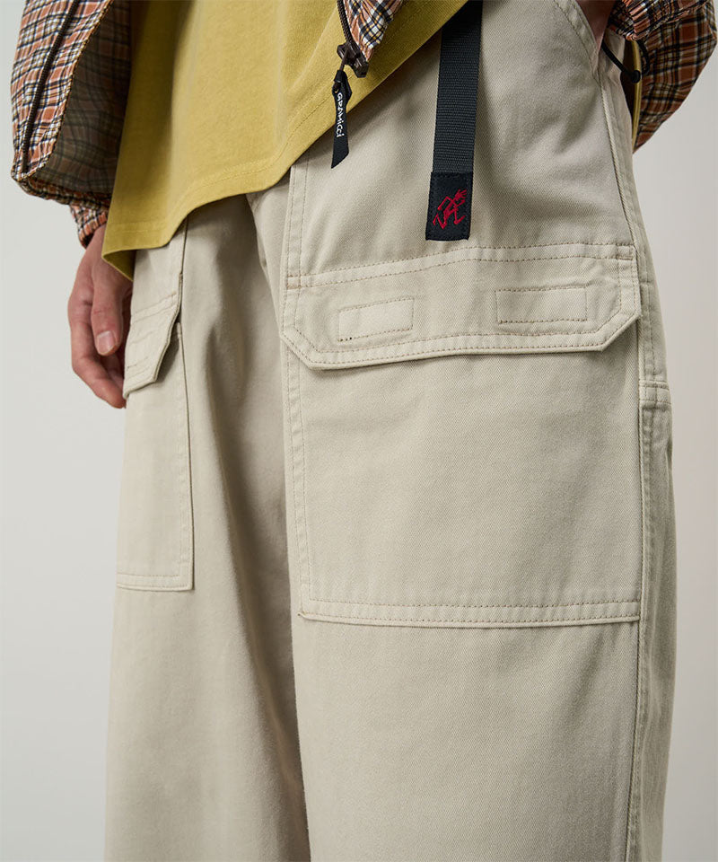 Model wearing sand pigment Gramicci EQT Pant and a plaid jacket on a light-tone background.