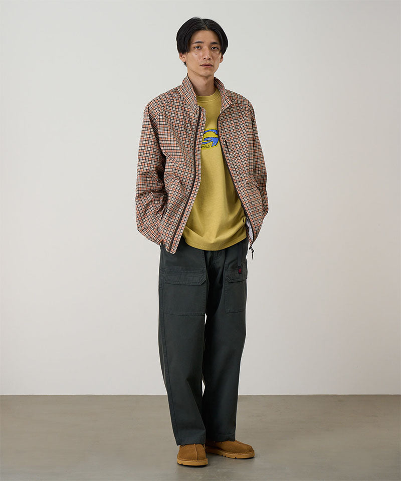 Model wearing smokey grey Gramicci EQT Pant and a plaid jacket on a light-tone background.