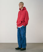 Model wearing light wash colored Gramicci Denim EQT Pant and a red hoodie on a light-tone background.