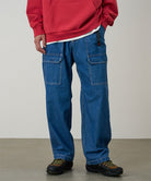 Model wearing light wash colored Gramicci Denim EQT Pant and a red hoodie on a light-tone background.
