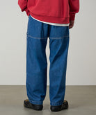 Back view of a model wearing light wash colored Gramicci Denim EQT Pant and a red hoodie on a light-tone background.