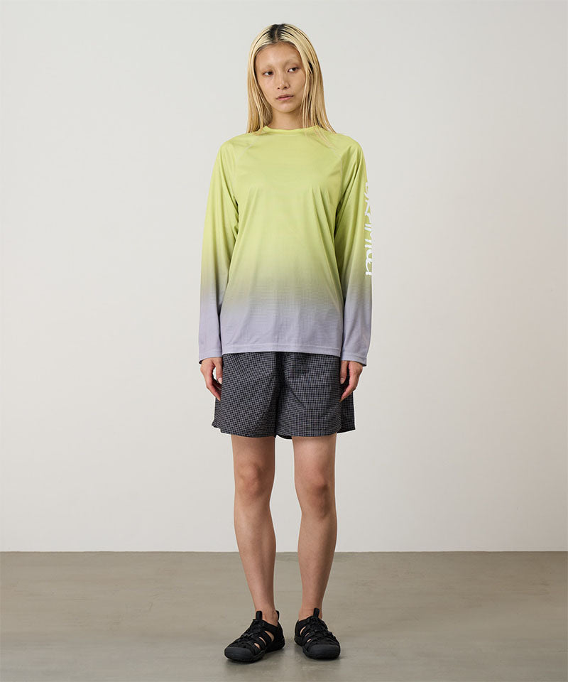 Model wearing a yellow gradient Gramicci UPF Shield S/S Top with a sleeve graphic and black shorts on a light-tone background.

