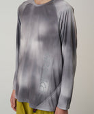 Model wearing a Gramicci black tie-dye L/S 1st Layer shirt with grey graphic against a light-tone background.