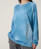 Model wearing a Gramicci blue tie-dye L/S 1st Layer shirt with grey graphic against a light-tone background.
