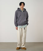 Model wearing a charcoal Gramicci G-Sail Zip Hooded Sweatshirt with a light grey graphic and light colored pants on a light-tone background.