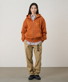 Model wearing a orange Gramicci G-Sail Zip Hooded Sweatshirt with a light orange graphic and light colored pants on a light-tone background.