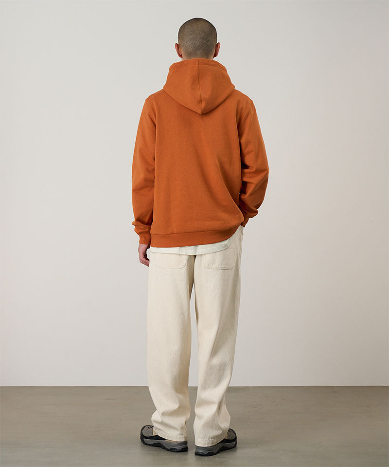 Back view of a model wearing the Gramicci Blueberry Hooded Sweatshirt  in orange with cream colored pants on a light tone background.
