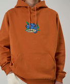 Gramicci Blueberry Hooded Sweatshirt with blueberry graphic in orange worn by a model against a light tone background.
