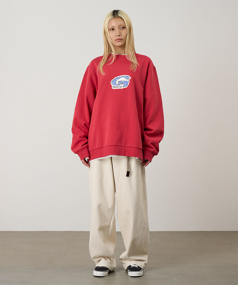 Model wearing a crimson red Gramicci G-Scribble Sweatshirt with a blue graphic and beige pants on a light tone background.