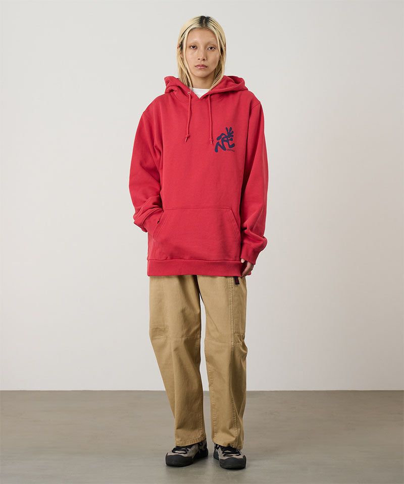 Model wearing a crimson red Gramicci Running Man Hooded Sweatshirt with a blue running man graphic and beige pants on a light tone background.