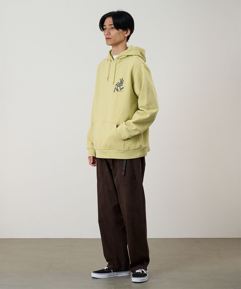 Model wearing a lime Gramicci Running Man Hooded Sweatshirt with a grey running man graphic and brown pants on a light tone background.