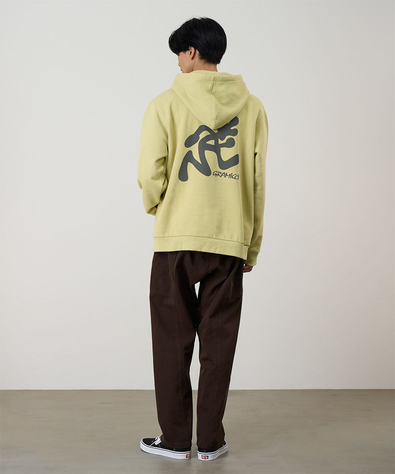 Back view of a model wearing a lime Gramicci Running Man Hooded Sweatshirt with a grey running man graphic and brown pants on a light tone background.