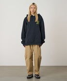 Model wearing a vintage black Gramicci Running Man Hooded Sweatshirt with an olive green graphic and khaki pants on a light-tone background.