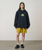 Model wearing a vintage black Gramicci Turtle Hooded Sweatshirt with a turtle graphic and yellow shorts on a light tone background.