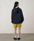 Back view of a model wearing a vintage black Gramicci Turtle Hooded Sweatshirt and yellow shorts on a light tone background.