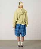 Person wearing a light green hoodie and blue plaid shorts standing against a plain background