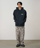 Model wearing a vintage black Gramicci Half Dome Hooded Sweatshirt with a beige and green graphic and camouflage pants on a light tone background.