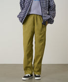Model wearing grass colored Gramicci Swell Pant and a plaid jacket on a light-tone background.