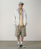Model wearing shadow plaid colored Gramicci Swell Short Shadow Plaid and a off-white jacket on a light-tone background.