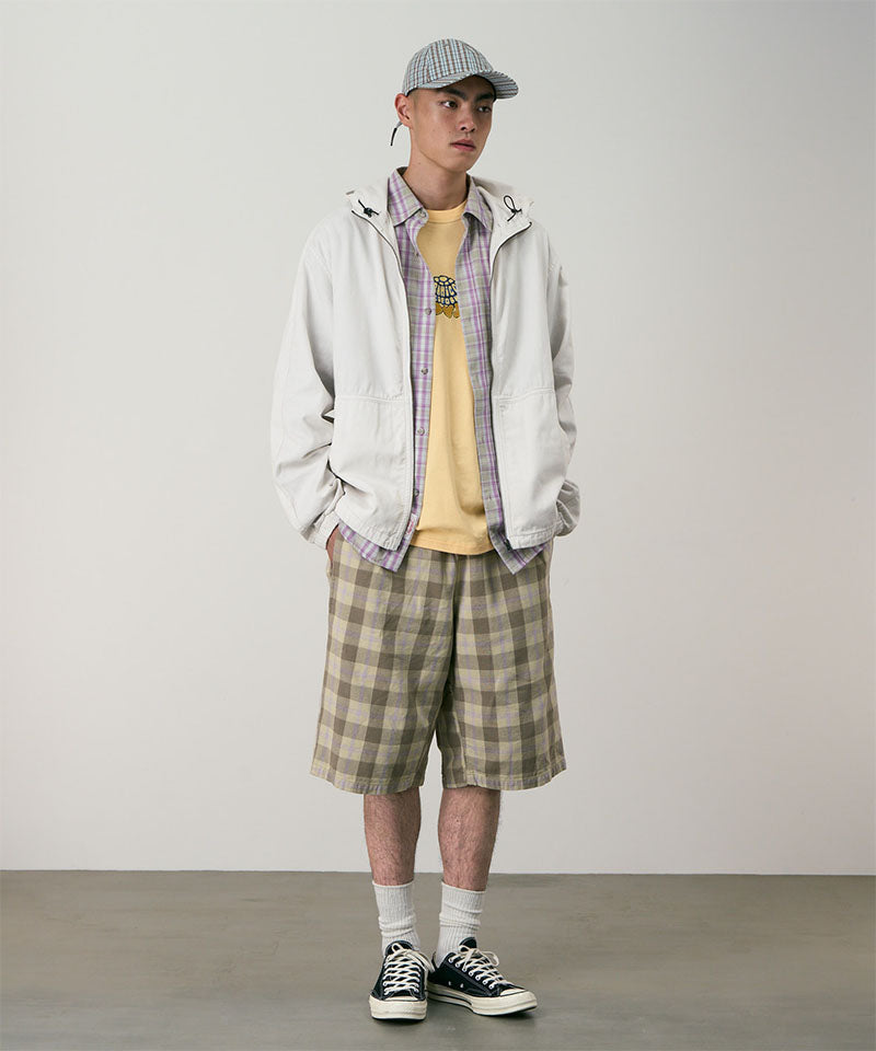 Model wearing shadow plaid colored Gramicci Swell Short Shadow Plaid and a off-white jacket on a light-tone background.