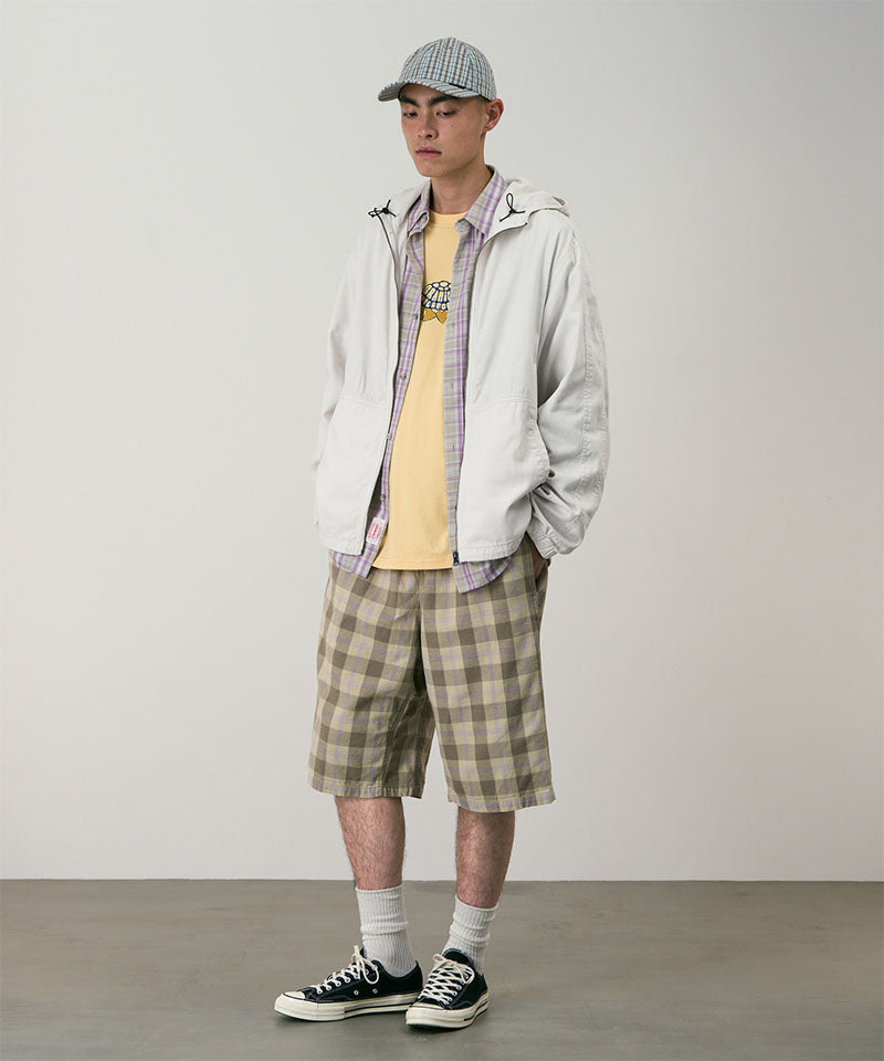 Model wearing shadow plaid colored Gramicci Swell Short Shadow Plaid and a off-white jacket on a light-tone background.