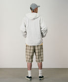 Back view of a model wearing shadow plaid colored Gramicci Swell Short Shadow Plaid and a off-white jacket on a light-tone background.