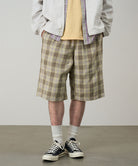 Model wearing shadow plaid colored Gramicci Swell Short Shadow Plaid and a off-white jacket on a light-tone background.