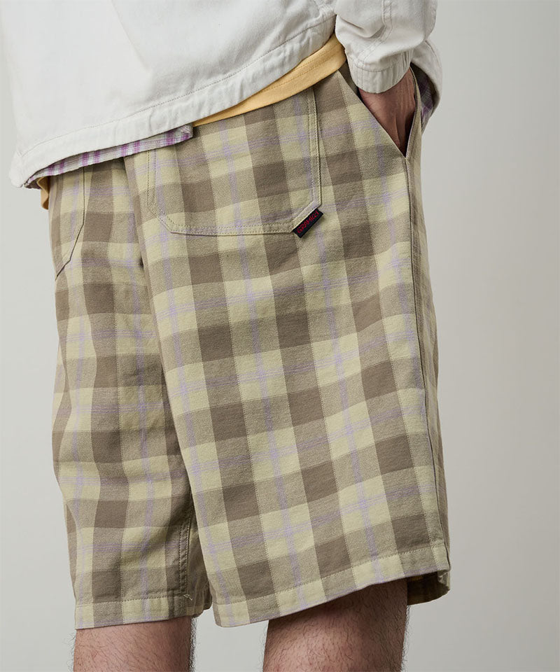 Back view of a model wearing shadow plaid colored Gramicci Swell Short Shadow Plaid and a off-white jacket on a light-tone background.