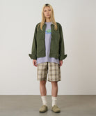 Model wearing shadow plaid colored Gramicci Swell Short Shadow Plaid and a olive jacket on a light-tone background.