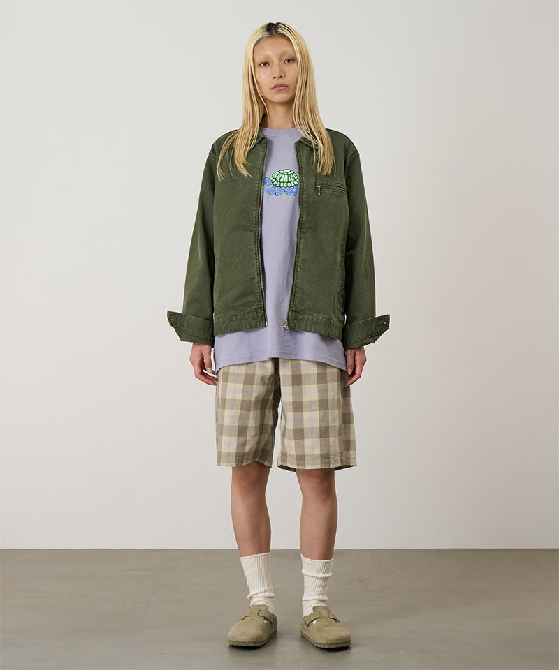 Model wearing shadow plaid colored Gramicci Swell Short Shadow Plaid and a olive jacket on a light-tone background.