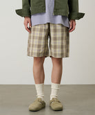 Model wearing shadow plaid colored Gramicci Swell Short Shadow Plaid and a olive jacket on a light-tone background.