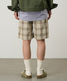 Back view of a model wearing shadow plaid colored Gramicci Swell Short Shadow Plaid and a olive jacket on a light-tone background.