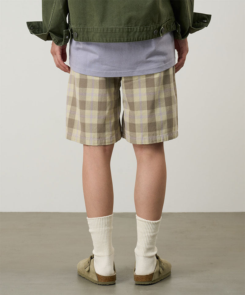 Back view of a model wearing shadow plaid colored Gramicci Swell Short Shadow Plaid and a olive jacket on a light-tone background.