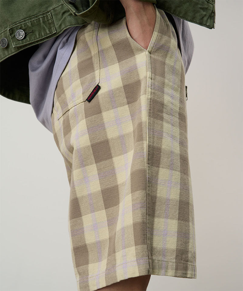 Model wearing shadow plaid colored Gramicci Swell Short Shadow Plaid and a olive jacket on a light-tone background.