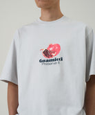 Model wearing a Gramicci smoke colored Pomegranate Tee with a graphic against a light tone background.
