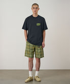 Model wearing a vintage black Gramicci G-Sail Tee with a yellow graphic and green plaid pants on a light-tone background.