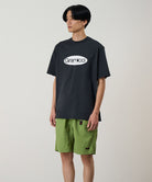 Model wearing a vintage black Gramicci Outdoor Gear Tee with a light beige graphic and green shorts on a light-tone background.