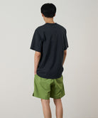 Back view of a model wearing a vintage black Gramicci Outdoor Gear Tee and green shorts on a light-tone background.