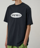 Model wearing a Gramicci vintage black Outdoor Gear Tee with a light beige graphic against a light-tone background.