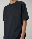 Model wearing a black Gramicci Running Man Tee with graphic against a light tone background.
