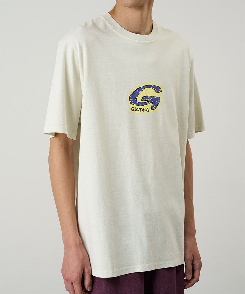 Model wearing a Gramicci natural colored G-Scribble Tee Pigment Dyed shirt with a purple graphic against a light tone background.
