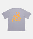 Back view of a Gramicci lavender Running Man Tee with dark mango colored graphic against a light-tone background.