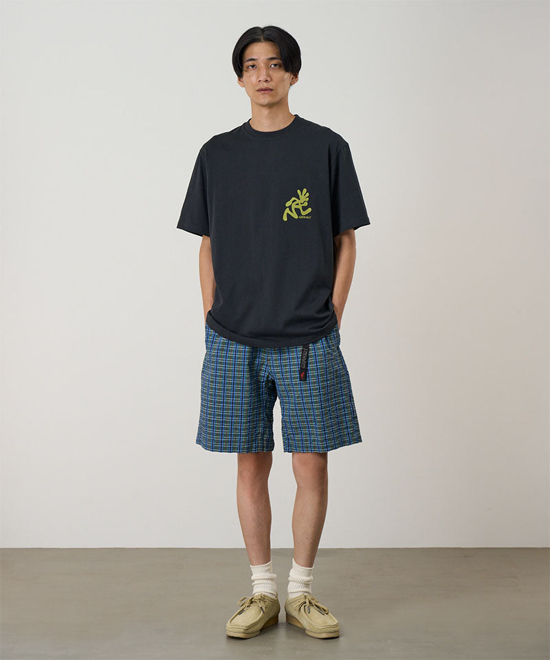 Model wearing a vintage black Gramicci Running Man Tee with lime green graphic and blue plaid shorts on a light-tone background.