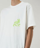 Model wearing a Gramicci white Running Man Tee with lime green graphic against a light-tone background.
