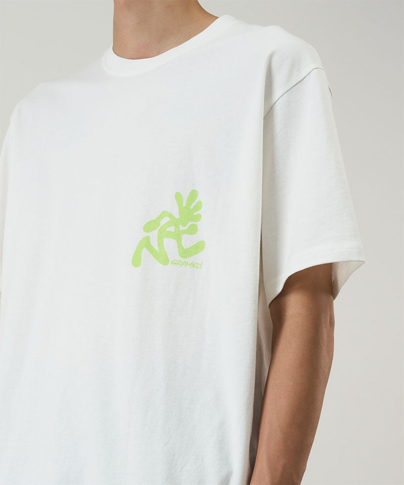 Model wearing a Gramicci white Running Man Tee with lime green graphic against a light-tone background.