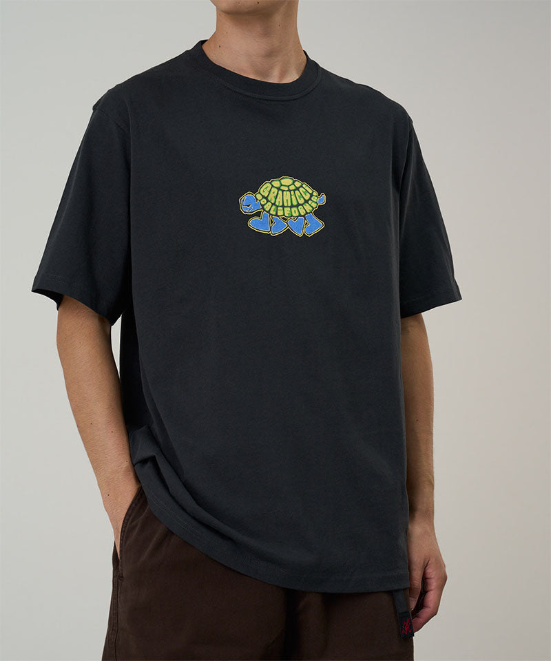 Model wearing a Gramicci vintage black Turtle Tee with a turtle graphic against a light tone background.
