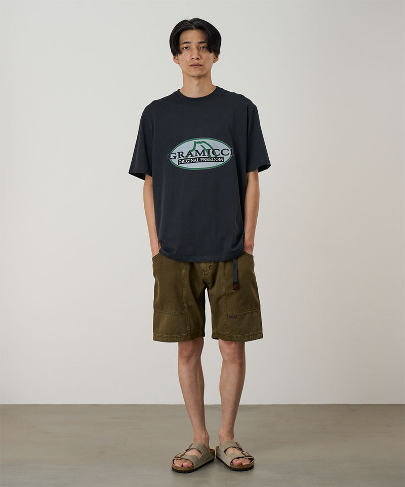 Model wearing a vintage black Gramicci Half Dome Tee with a grey graphic and green shorts on a light tone background.
