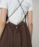 Back view of a model wearing a Gramicci Women's Woven Milton Dress in the color walnut and a white undershirt on a light-tone background.
