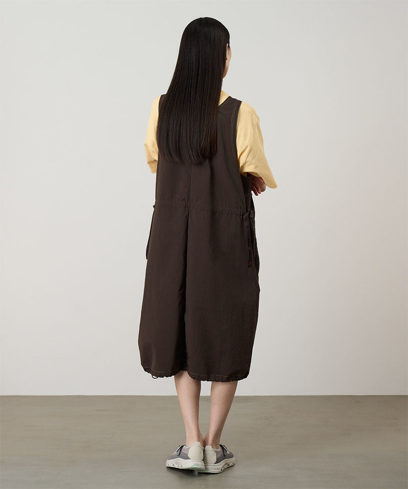 Back view of a model wearing a chocolate colored Gramicci Nylon Dress and a yellow shirt on a light-tone background.